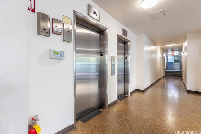 corridor featuring baseboards, dark speckled floor, and elevator