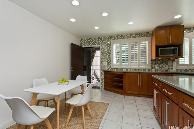 kitchen with light tile patterned floors, tasteful backsplash, stainless steel microwave, and brown cabinets