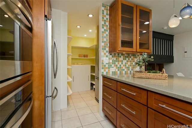 kitchen featuring brown cabinetry, decorative backsplash, light stone countertops, stainless steel appliances, and light tile patterned flooring