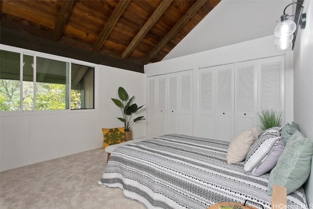 bedroom featuring lofted ceiling with beams, wood ceiling, multiple closets, and carpet flooring