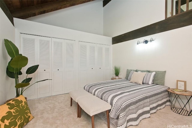 carpeted bedroom with high vaulted ceiling, beamed ceiling, and two closets