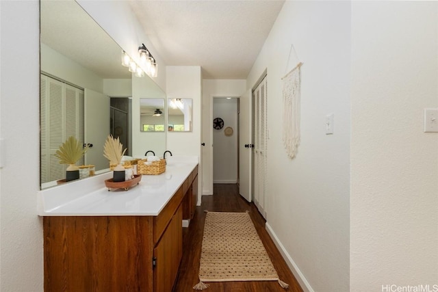 bathroom with wood finished floors, a shower, baseboards, ceiling fan, and vanity