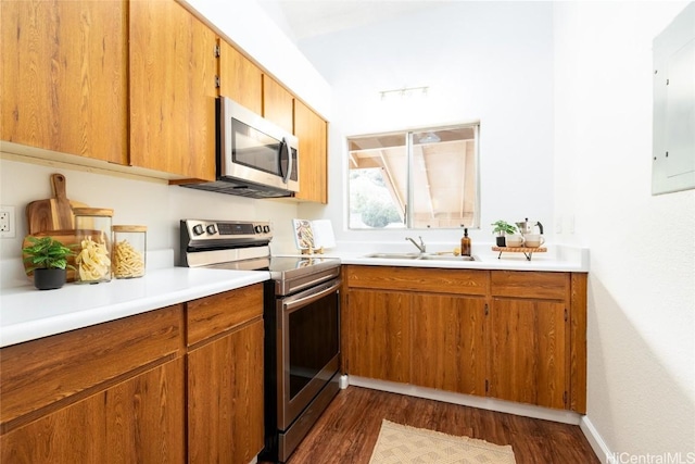 kitchen with brown cabinets, a sink, dark wood finished floors, stainless steel appliances, and light countertops