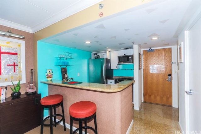 kitchen featuring a breakfast bar, stainless steel microwave, ornamental molding, freestanding refrigerator, and a peninsula