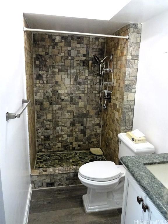 bathroom featuring wood finished floors, a shower stall, toilet, and vanity