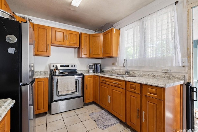 kitchen with light tile patterned floors, a sink, appliances with stainless steel finishes, a textured ceiling, and brown cabinets