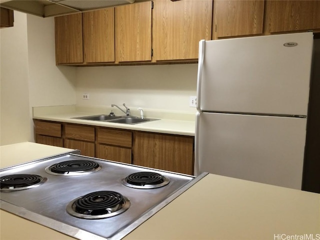 kitchen with light countertops, range, freestanding refrigerator, brown cabinetry, and a sink