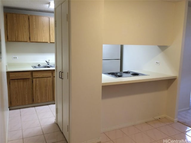 kitchen with brown cabinets, a sink, electric stovetop, freestanding refrigerator, and light countertops