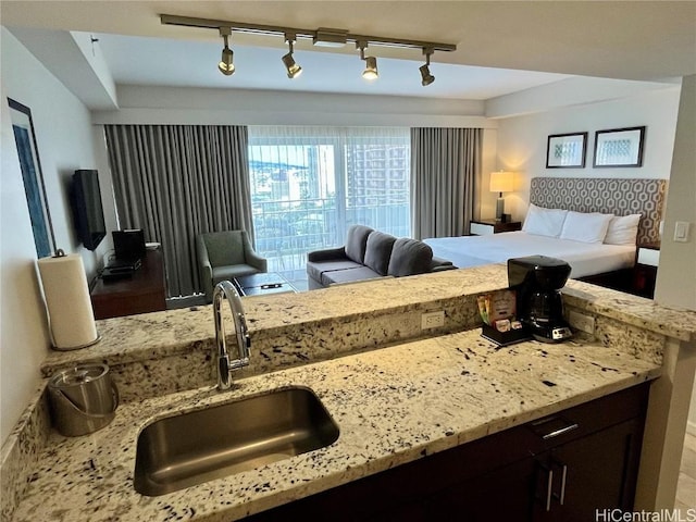 kitchen featuring open floor plan, light stone counters, a sink, and dark brown cabinetry