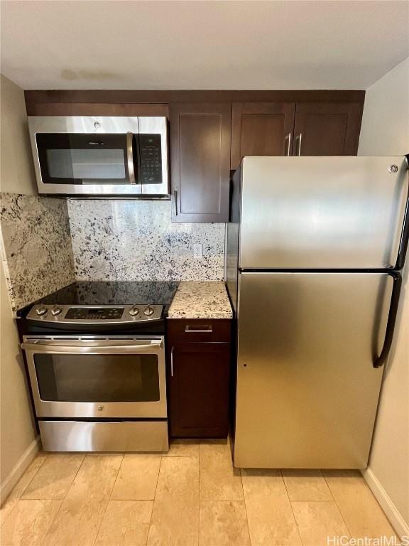 kitchen with light stone counters, dark brown cabinetry, baseboards, appliances with stainless steel finishes, and backsplash