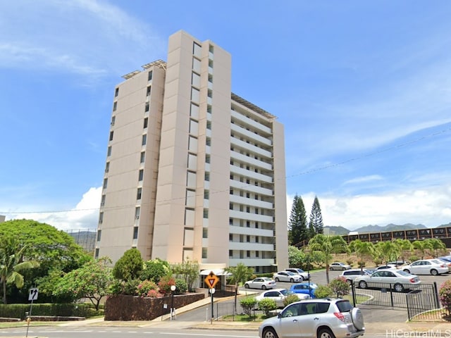 view of building exterior with fence, a mountain view, and uncovered parking