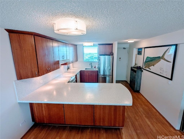 kitchen with brown cabinetry, wood finished floors, a peninsula, freestanding refrigerator, and light countertops