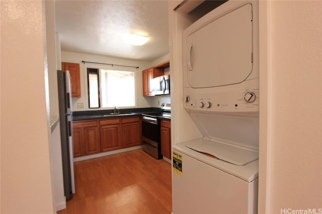 kitchen featuring brown cabinets, a sink, stacked washer and clothes dryer, appliances with stainless steel finishes, and light wood-type flooring