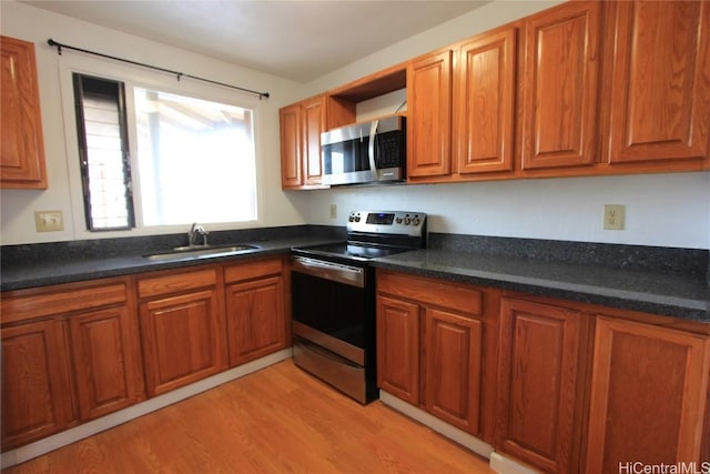 kitchen featuring dark countertops, light wood-type flooring, brown cabinetry, stainless steel appliances, and a sink