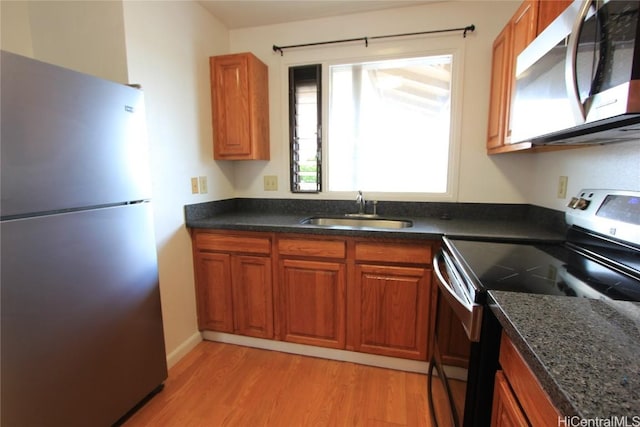 kitchen featuring light wood finished floors, brown cabinetry, appliances with stainless steel finishes, and a sink