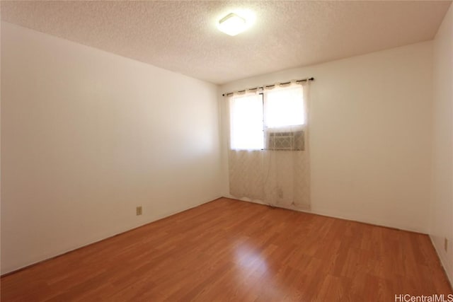 empty room featuring cooling unit, a textured ceiling, and light wood-type flooring