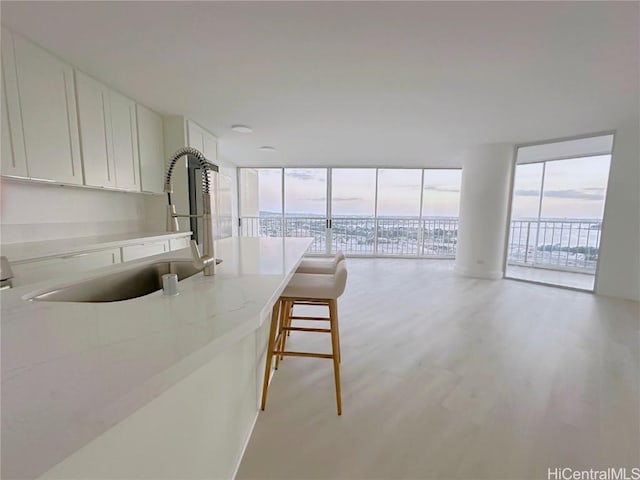 kitchen featuring light wood-style floors, open floor plan, white cabinetry, a sink, and a wall of windows