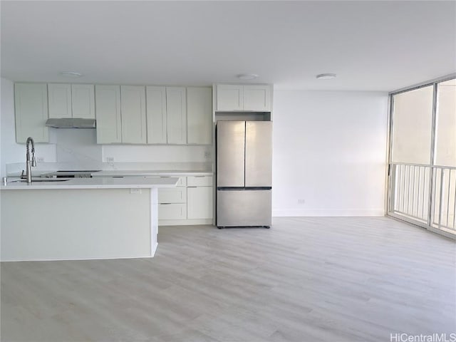 kitchen with freestanding refrigerator, light countertops, light wood-type flooring, under cabinet range hood, and a sink