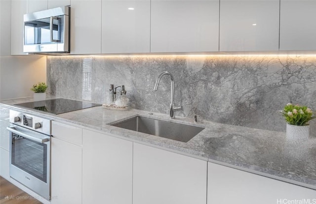 kitchen featuring a sink, light stone counters, modern cabinets, and stainless steel appliances