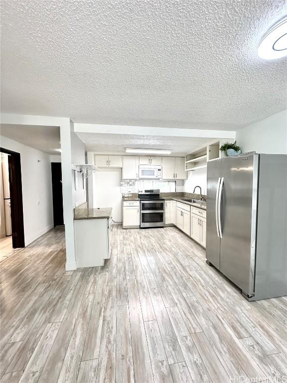 kitchen with a sink, dark countertops, a textured ceiling, light wood-style floors, and appliances with stainless steel finishes