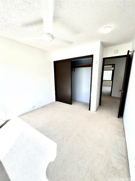 bedroom featuring light colored carpet, a textured ceiling, a closet, and a ceiling fan