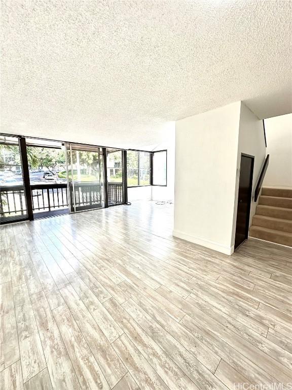 unfurnished room featuring light wood finished floors, stairway, a textured ceiling, and expansive windows