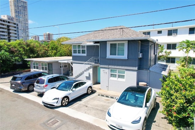 multi unit property featuring a view of city, uncovered parking, a shingled roof, and stairway