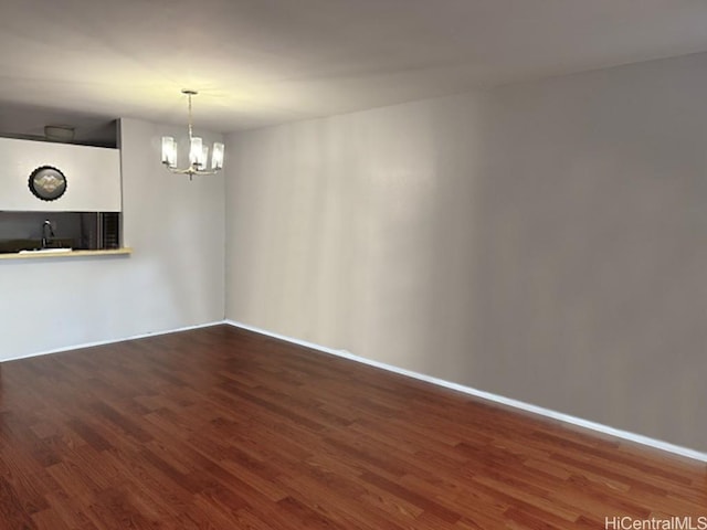 spare room with a chandelier, a sink, baseboards, and wood finished floors