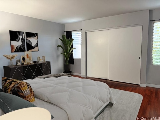 bedroom with a closet, multiple windows, baseboards, and wood finished floors