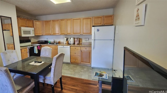 kitchen with light brown cabinets, a sink, a textured ceiling, wood finished floors, and white appliances