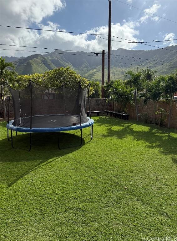 view of yard with a trampoline, a mountain view, and fence