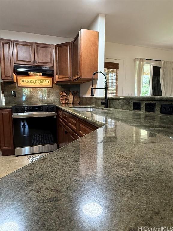 kitchen featuring electric range, a sink, backsplash, range hood, and dark stone countertops