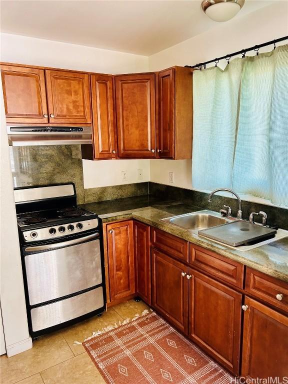 kitchen with brown cabinets, light tile patterned floors, a sink, gas range, and under cabinet range hood