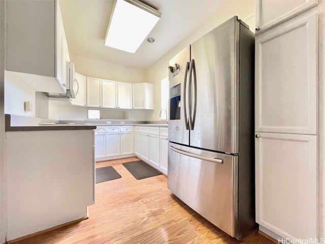 kitchen with stainless steel fridge, white cabinets, white microwave, light wood-style flooring, and a sink