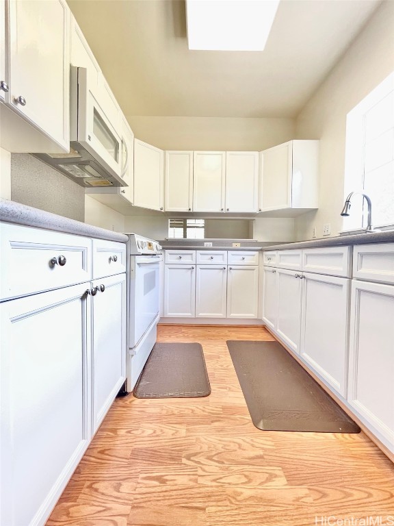 kitchen with white appliances, a skylight, white cabinets, light countertops, and light wood-type flooring