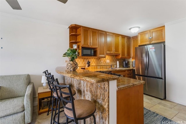 kitchen featuring black microwave, a peninsula, freestanding refrigerator, tasteful backsplash, and crown molding