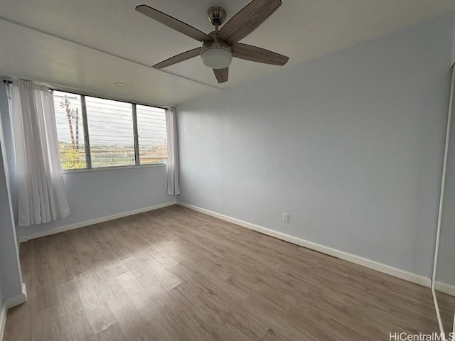 empty room with wood finished floors, a ceiling fan, and baseboards