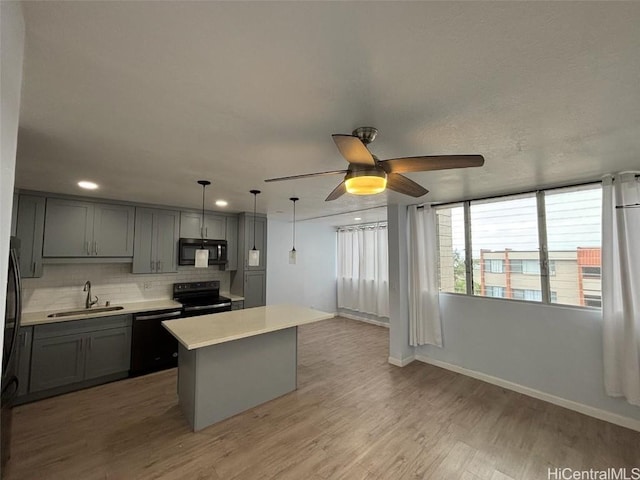 kitchen featuring gray cabinets, light countertops, a sink, light wood-type flooring, and black appliances