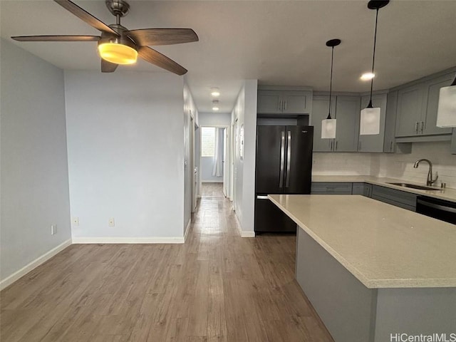 kitchen featuring gray cabinetry, light countertops, a sink, and freestanding refrigerator