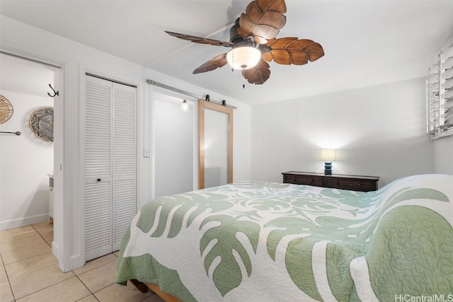 bedroom featuring a barn door, baseboards, ceiling fan, tile patterned floors, and a closet