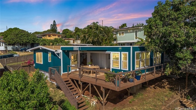 back of property at dusk with a deck and fence