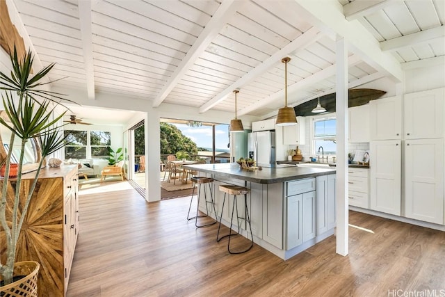 kitchen featuring light wood-type flooring, lofted ceiling with beams, a kitchen island, dark countertops, and stainless steel fridge with ice dispenser