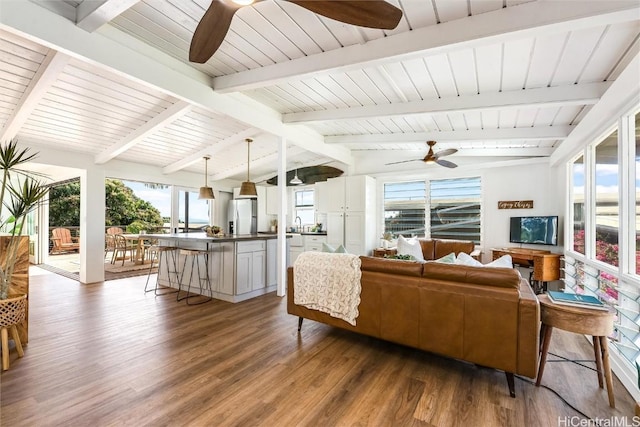 living area featuring wood finished floors, vaulted ceiling with beams, and a ceiling fan