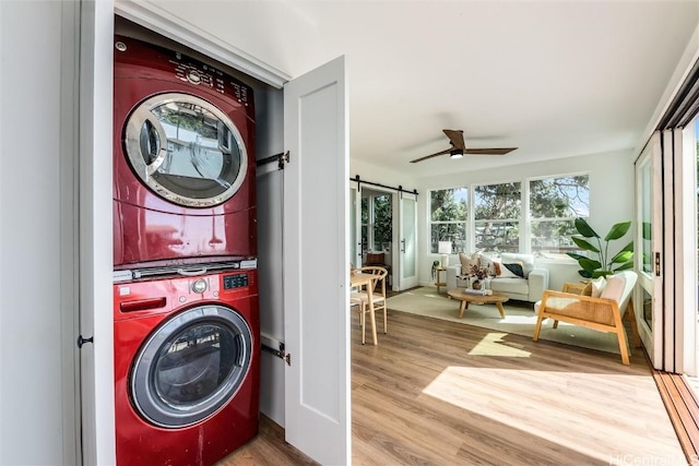 laundry area with a ceiling fan, wood finished floors, laundry area, stacked washer / drying machine, and a barn door