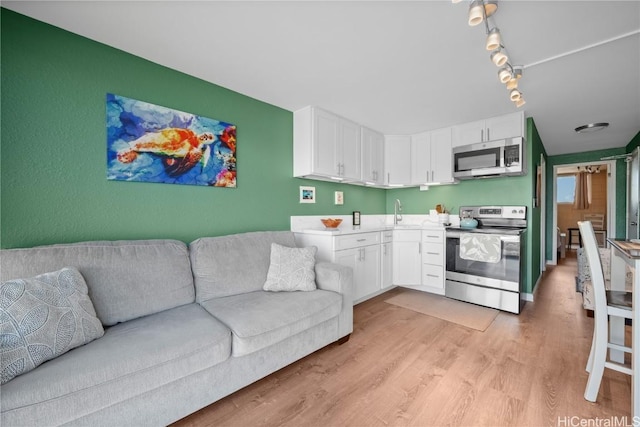 kitchen with open floor plan, white cabinetry, appliances with stainless steel finishes, light wood finished floors, and light countertops