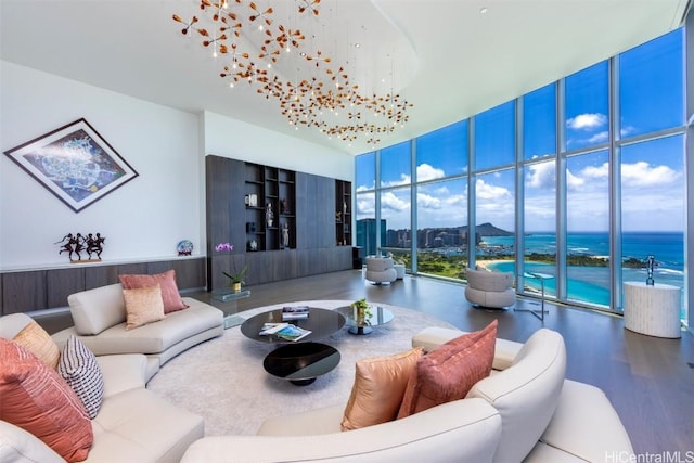 living room with a water view, a towering ceiling, floor to ceiling windows, and wood finished floors