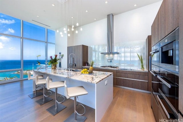 kitchen with modern cabinets, a kitchen breakfast bar, expansive windows, island exhaust hood, and stainless steel gas stovetop