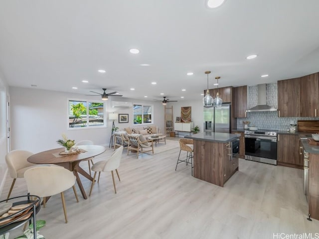 kitchen with a kitchen island, an AC wall unit, appliances with stainless steel finishes, dark countertops, and wall chimney exhaust hood