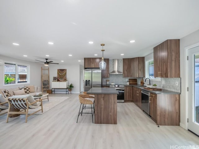 kitchen featuring a kitchen breakfast bar, dark countertops, a kitchen island, appliances with stainless steel finishes, and wall chimney exhaust hood