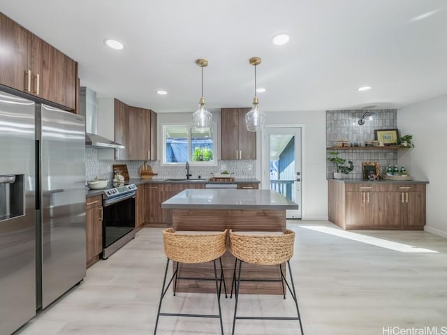 kitchen with a breakfast bar, a sink, tasteful backsplash, appliances with stainless steel finishes, and wall chimney range hood